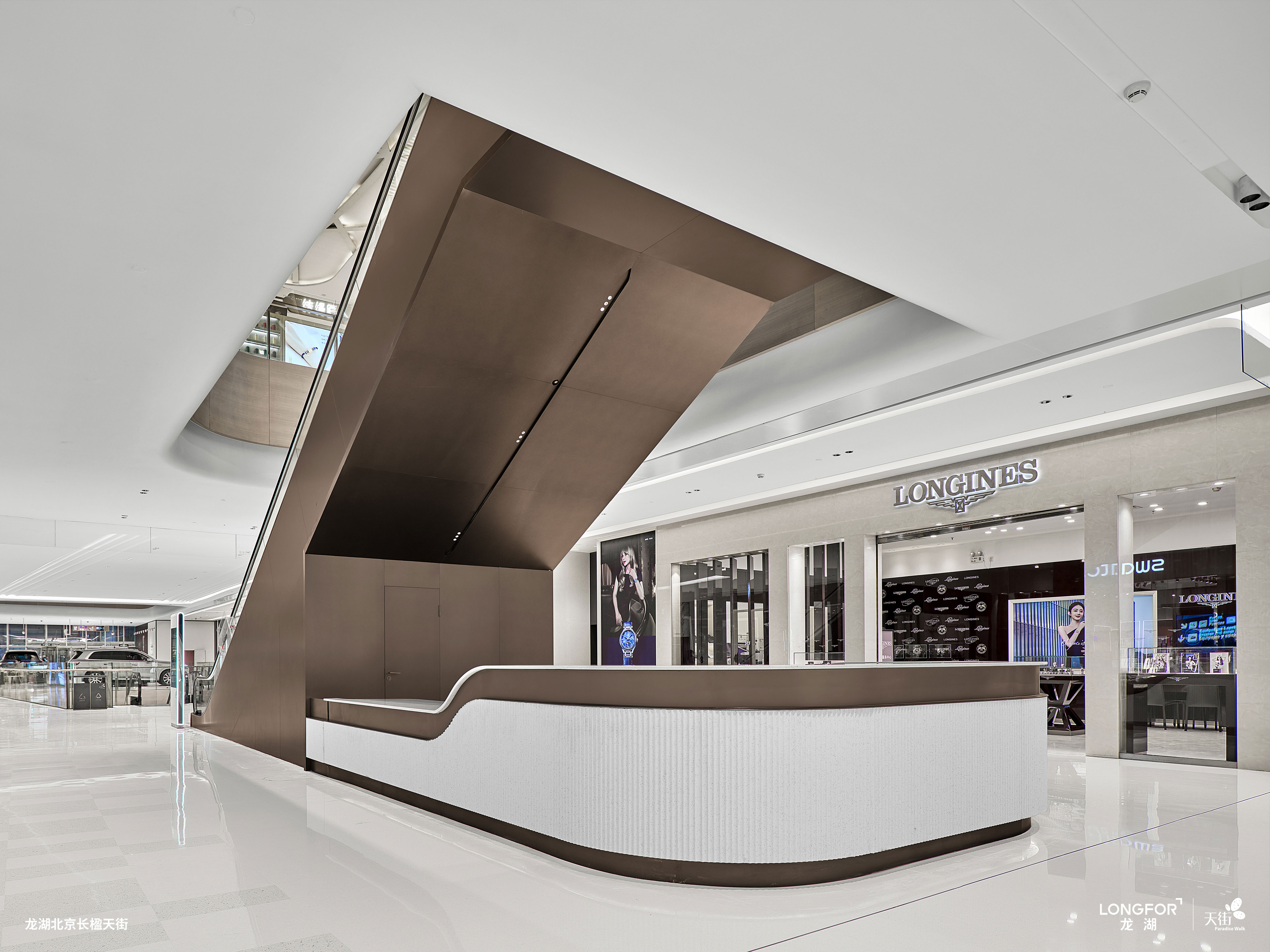 购物中心内现代圆形天花板，中央区域有三角形镜面装饰，周围环绕暖色灯光。