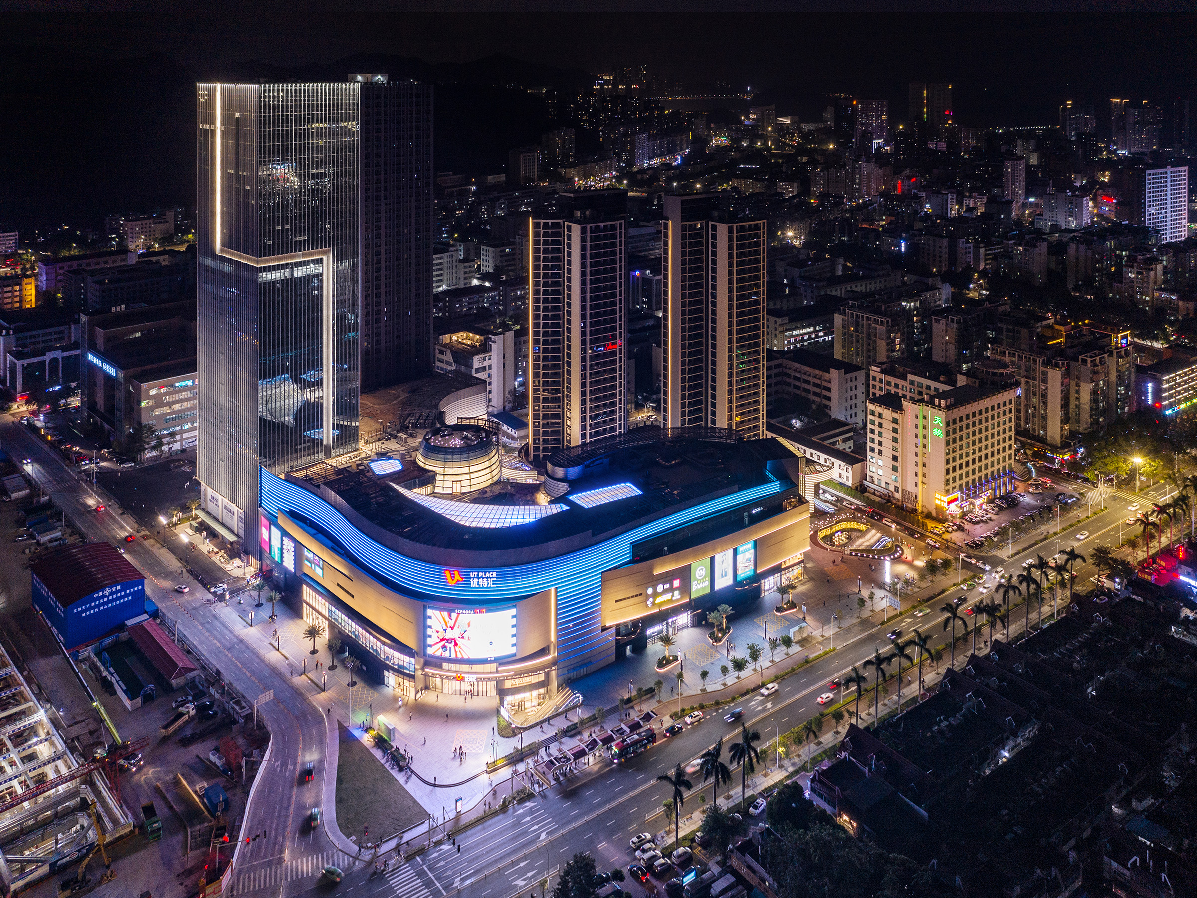 购物中心内现代圆形天花板，中央区域有三角形镜面装饰，周围环绕暖色灯光。