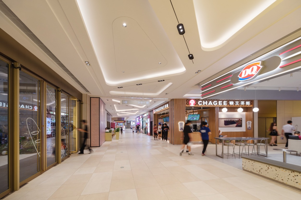 购物中心内现代圆形天花板，中央区域有三角形镜面装饰，周围环绕暖色灯光。