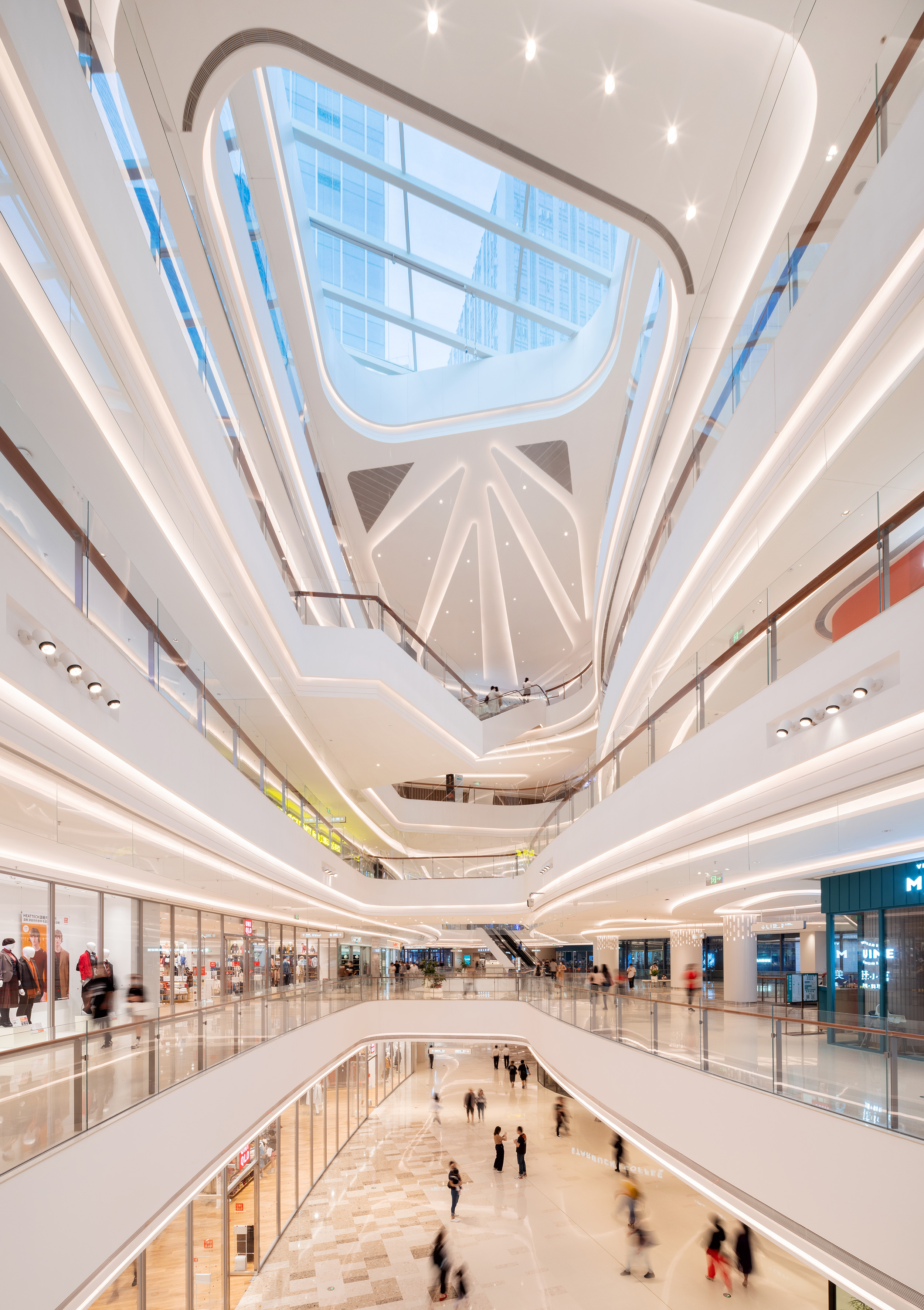 现代购物中心内部多层结构，透明玻璃天窗顶棚和扶梯连接各楼层。