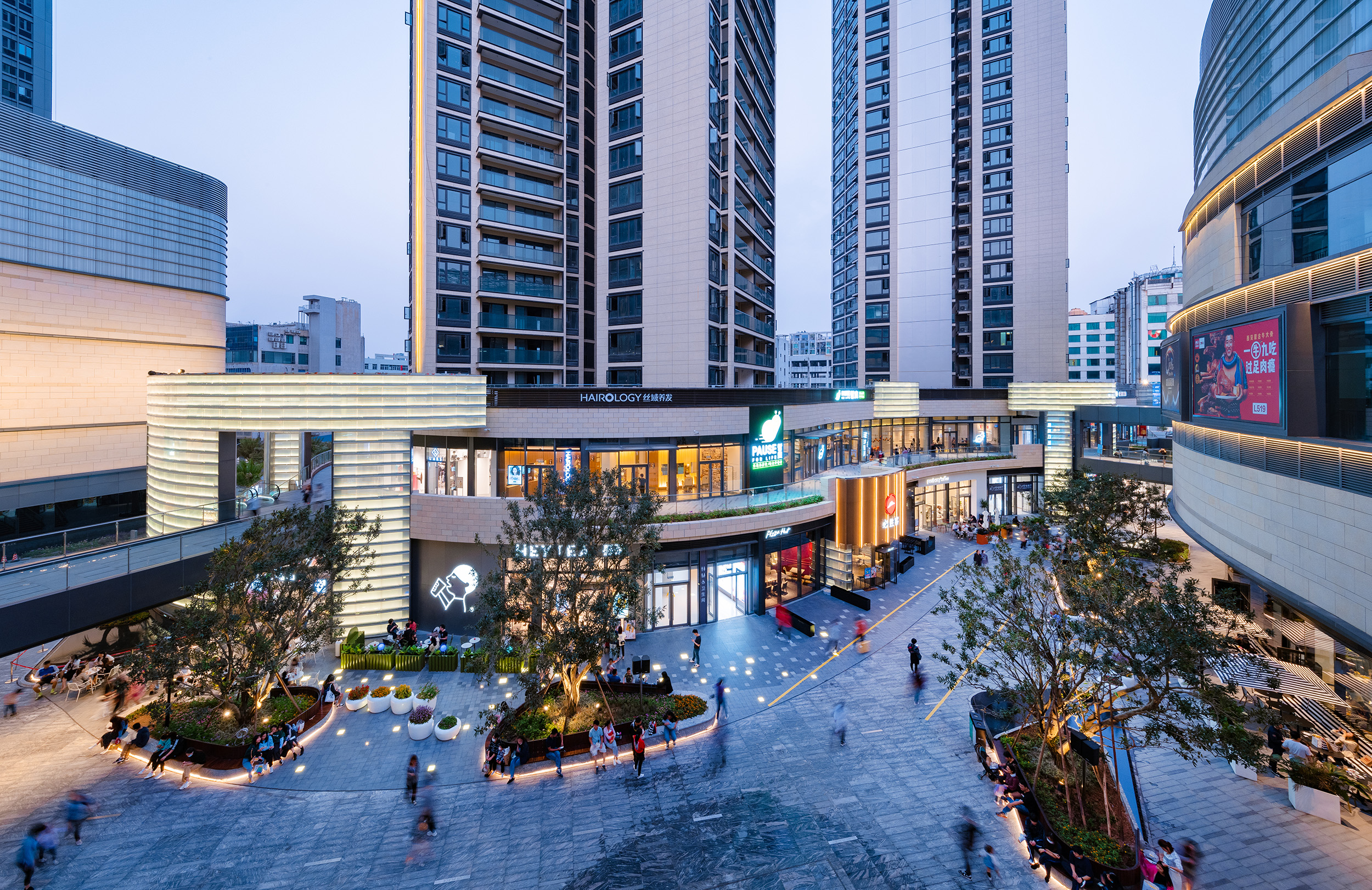 现代购物中心内，人们在明亮的走廊中行走，天花板装饰有圆环形灯光，商店包括Calvin Jeans和DISSONA。