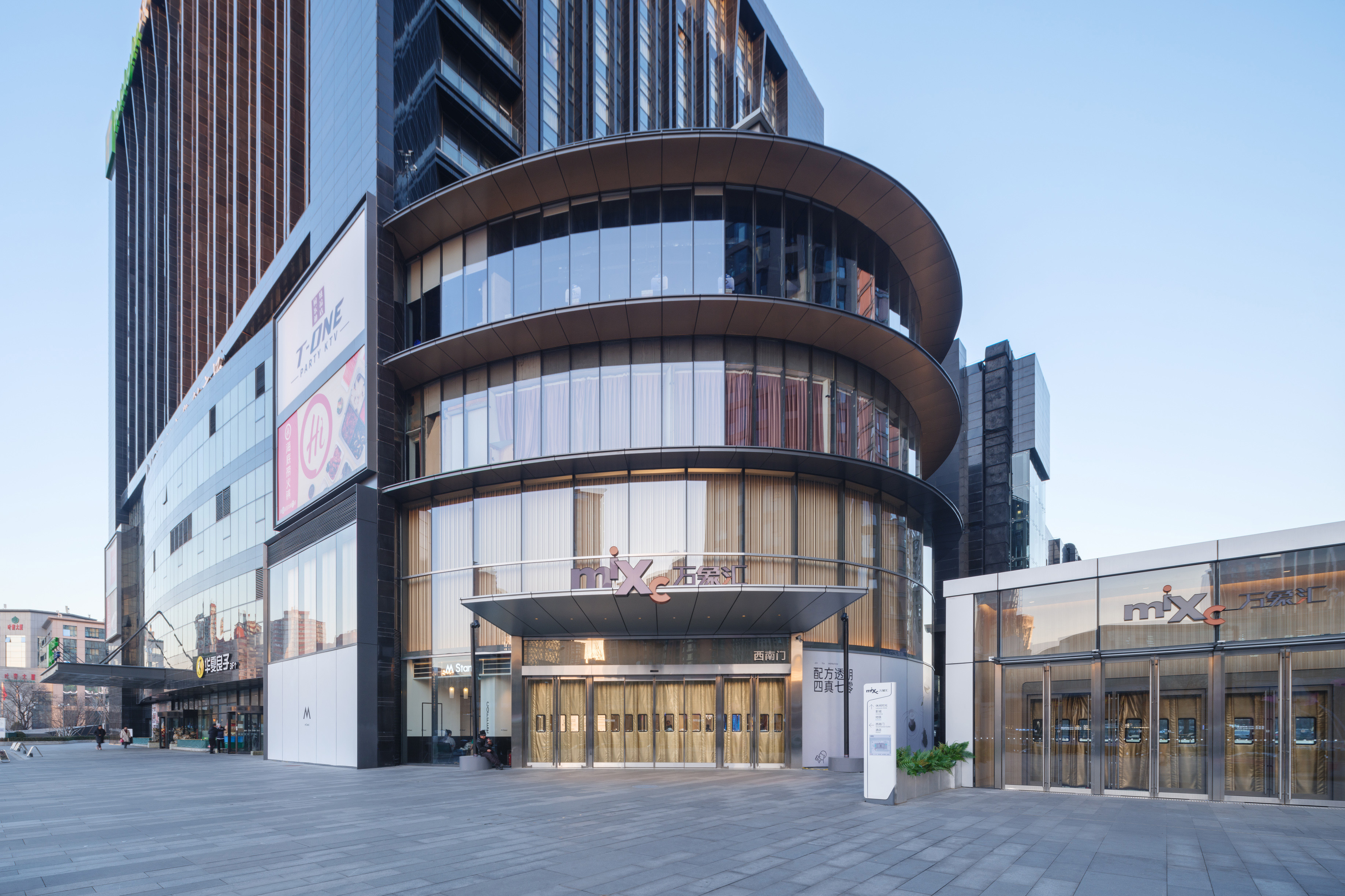 购物中心内现代圆形天花板，中央区域有三角形镜面装饰，周围环绕暖色灯光。