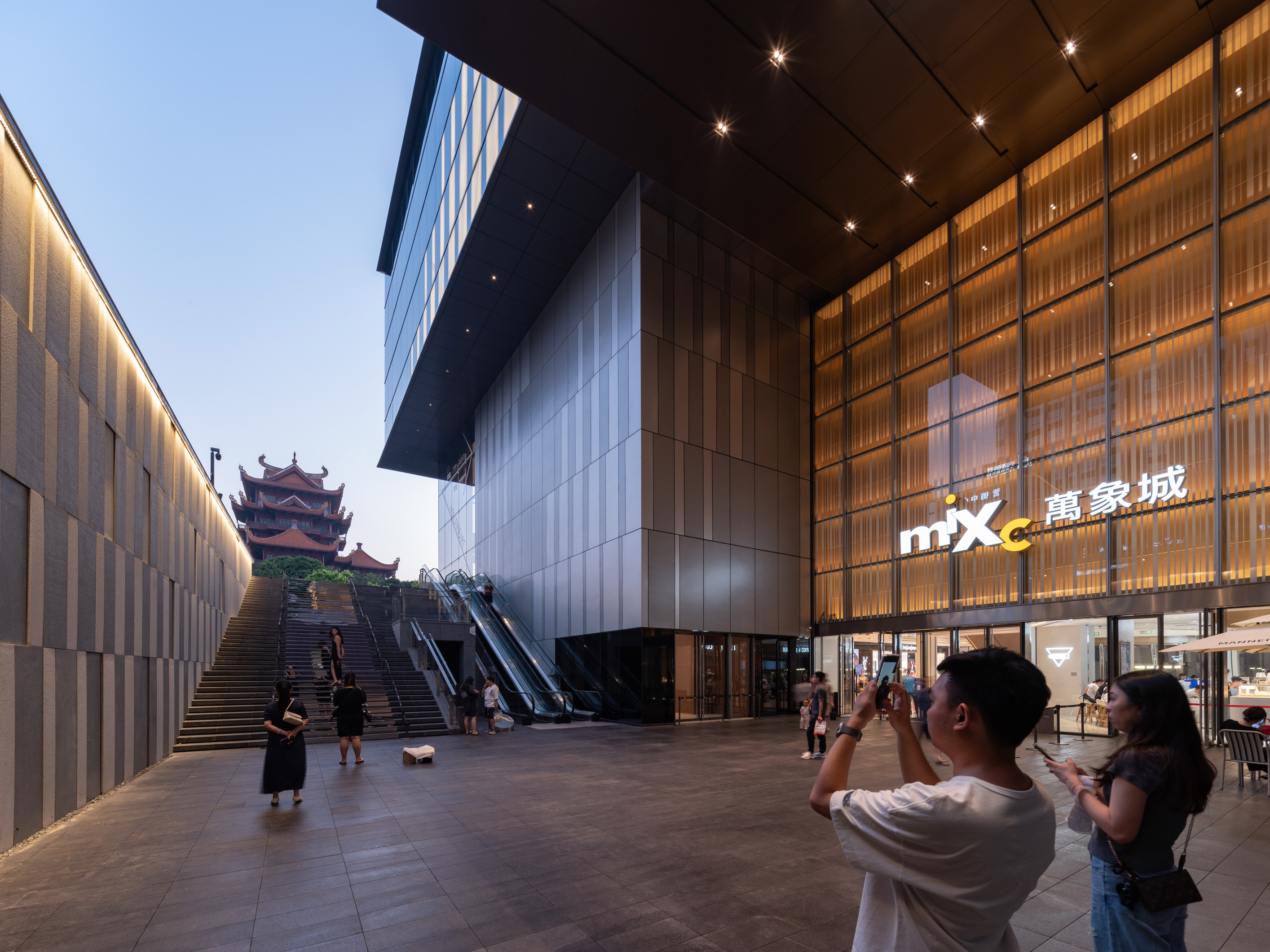 购物中心内现代圆形天花板，中央区域有三角形镜面装饰，周围环绕暖色灯光。