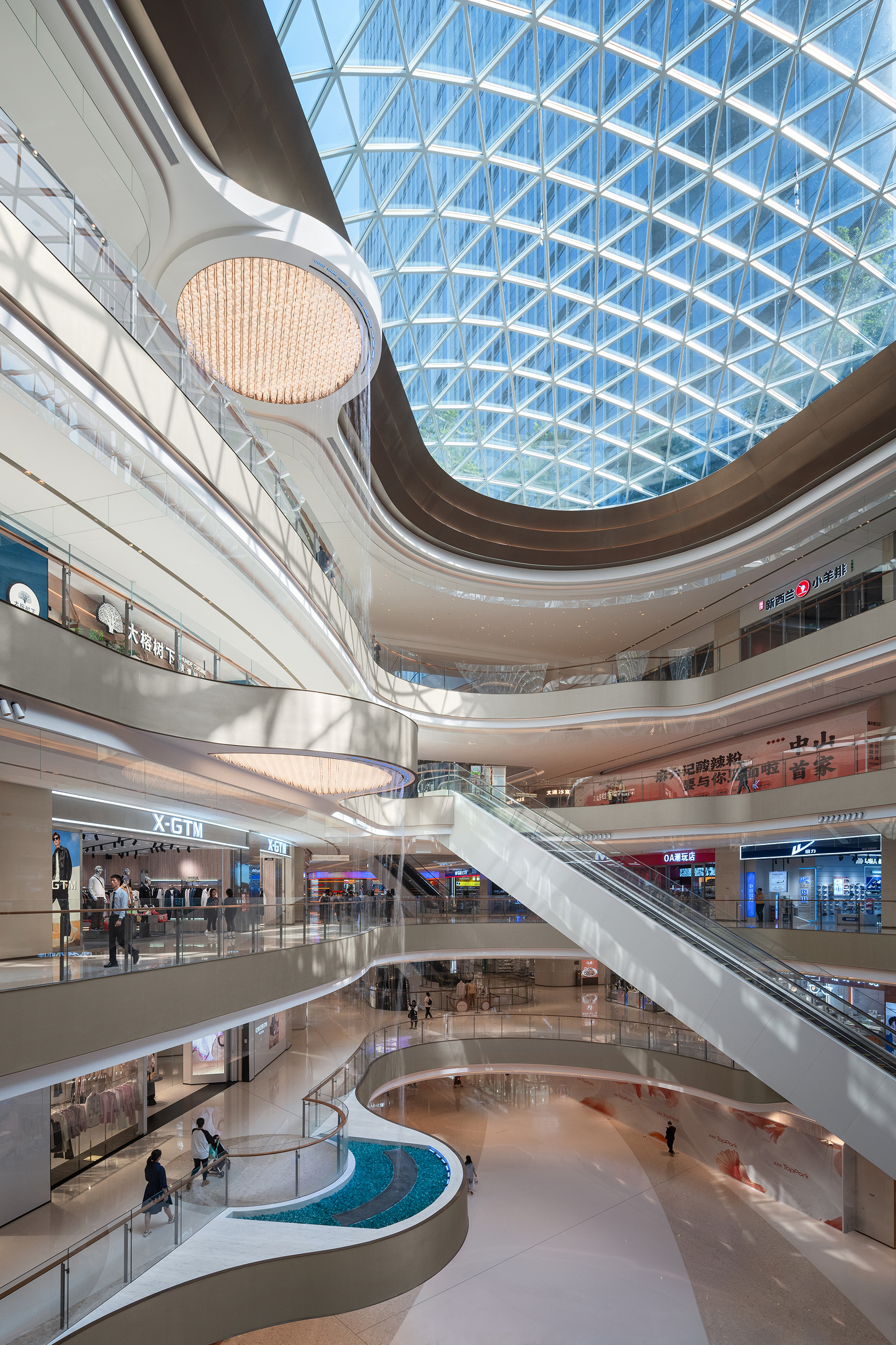 现代购物中心内部多层结构，透明玻璃天窗顶棚和扶梯连接各楼层。